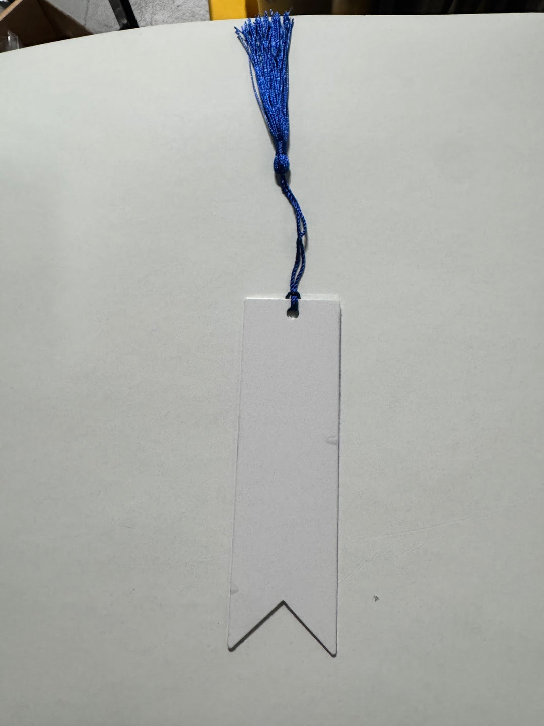 Blank white sublimation bookmark with a notched swallowtail bottom and a blue tassel
