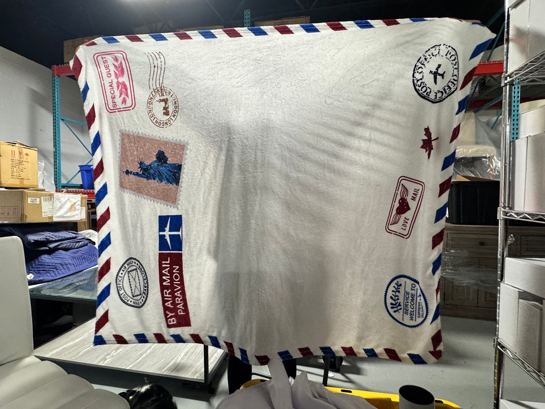 Cream plush fleece throw blanket printed with a vintage airmail envelope design and striped border