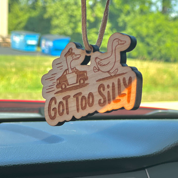 Wooden ornament with 'Got Too Silly' text and duck illustration on a car dashboard.
