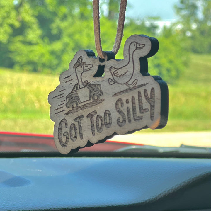 Wooden ornament with ducks and 'GOT TOO SILLY' text hanging from a car's rearview mirror.