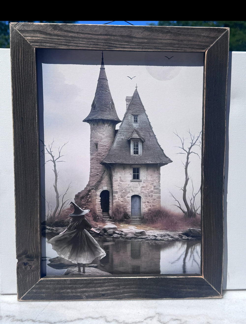 Framed print of a haunted house by a lake with a witch