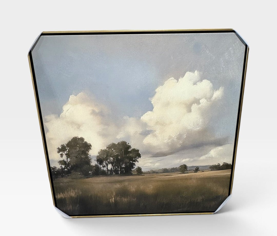 A square decorative tray with a gold-toned metal border, featuring a landscape painting of a grassy field under a cloudy blue sky, shown on a light gray background.