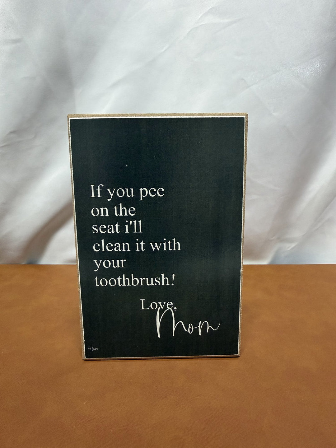 Wood sign joking about peeing on the toilet seat