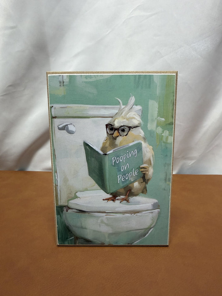 Wood print of a bird reading a book called Pooping on People
