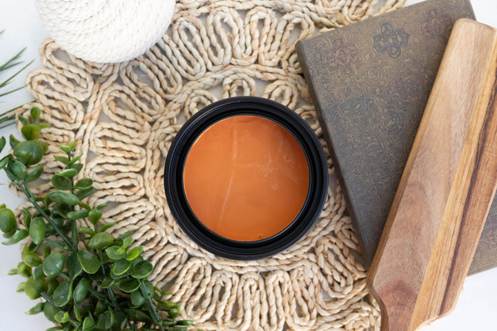 Open can of Marigold Terra Clay Paint styled on a wicker table with a book and ivy plant